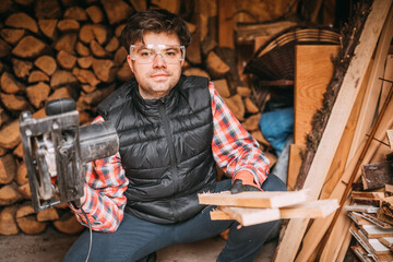 portrait of a handsome man cutting wood with a circular saw, cutting wood for the fireplace, shed with wood