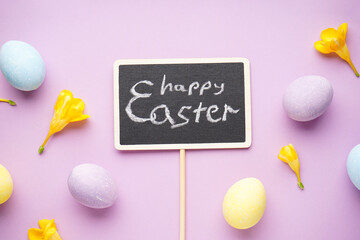 Easter eggs and freesia flowers on a purple background. Flat lay.