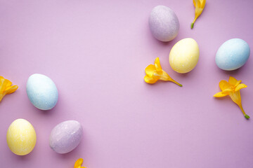 Easter eggs and freesia flowers on a purple background, place for text, top view.