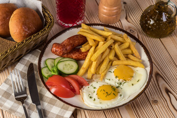 Fried sausages with fries, fried eggs and vegetables on a rustic background
