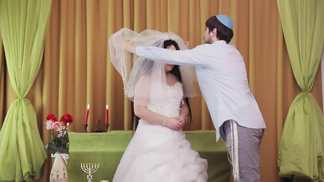 During the chuppah ceremony, the Jewish bride and groom in the synagogue lifts the veil from the bride's face. Medium plan