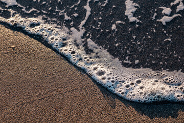A wave brings bubbles across the sand on a wet day