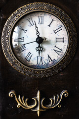 Close up image of an antique clock face and metal decoration below on a dark background. The time...