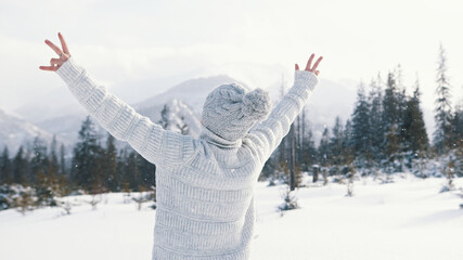 Young woman watching the snowfall and rising her hands on the mountain. High quality photo