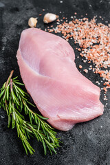 Raw Poultry turkey breast fillet meat on a butcher table with rosemary and salt. Black background. Top View