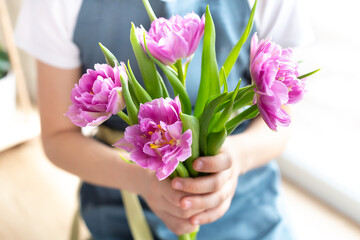 A bouquet of beautiful pink tulips in the hands of a girl in a blue apron. The concept of growing flowers, gardening and floristry. Flower shop. Spring interior decor. Give with love.