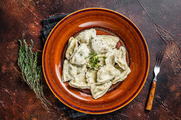 Polish Pierogi Dumplings with potato in a plate with herbs and butter. Dark background. Top View