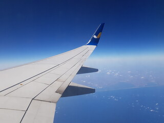 Obraz premium Aircraft Wing outside plane window on blue sky background, closeup