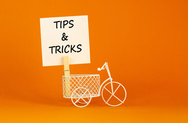 Fototapeta na wymiar Tips and tricks symbol. White paper. Words 'Tips and tricks'. Miniature bicycle. Beautiful orange background. Business and tips and tricks concept, copy space.