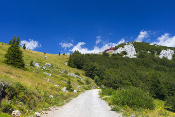 View to old meteorological station across green fields and rocky road in Northern Velebit National park