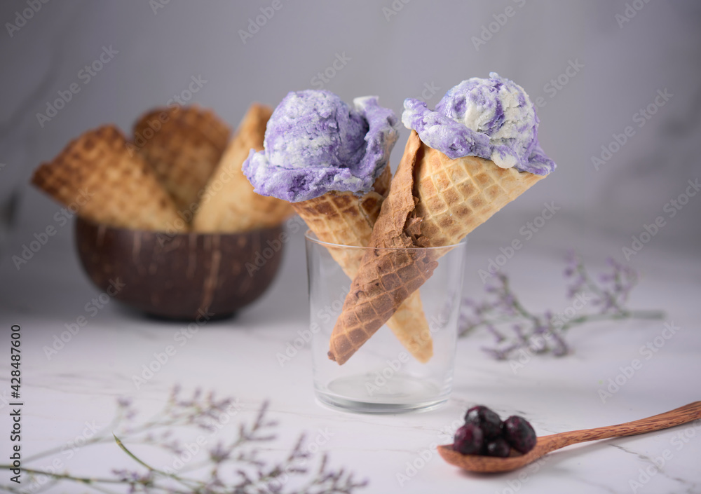 Sticker Closeup shot of two violet ice cream cones on a glass and a wooden spoon with berries