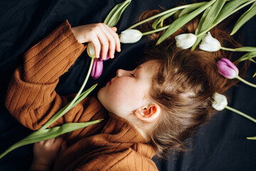 Naklejka premium The girl lies in tulips on a dark background. Happy Mother's Day