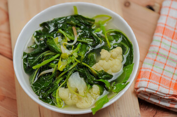 Sayur Bening Bayam or spinach clear soup with broccoli in a white bowl and wooden table