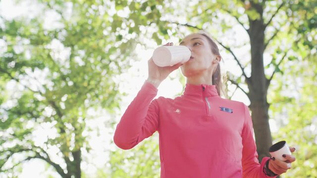 Fitness girl in pink sportswear drinking water from a bidon in the park