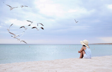 Fototapeta na wymiar Little cute girl in hat feeds seagulls on the beach.