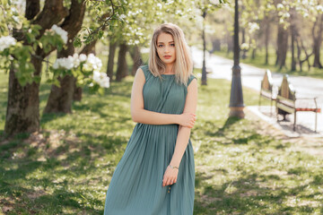 Beautiful blonde woman in a green long dress stays in a spring blooming garden.