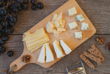 Cheese plate: Em mental, Camembert cheese, Parmesan, Blue cheese, crackers, walnuts, grapes on wooden table. Selective focus.