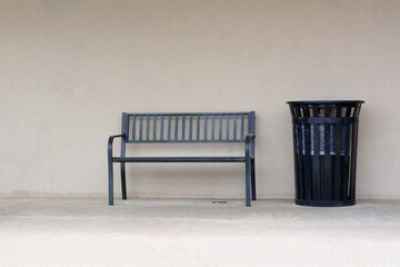 Urban bench and trash can in sidewalk against light brown office wall 