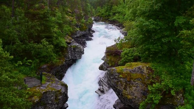 Stormy streams of water of the Slettafossen waterfall, which carved a channel in the rock. Rocky summer landscape of green forest. Norway.