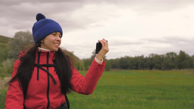 free Young girl tourist blogger records selfie videos at foot of mountains using a smartphone with a beautiful landscape in background. Healthy cheerful woman travels and photography nature by phone.