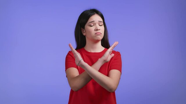 Pretty girl disapproving with no crossing hands sign make basta, negation, enough gesture. Denying, Rejecting, Disagree, Portrait of pretty girl on violet background