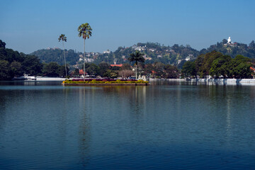 Fototapeta na wymiar Kandy, Sri lanka, 02/13/2014: Lake Kandy with the small island in the middle, the hills in the background with the Buddha statue of Bahiravakanda on the right