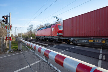 Selective focus view at red and white level crossing railway barrier which block the road and locomotive of freight train move on the rail on countryside in Germany.