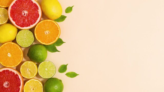 Fresh organic citrus fruits with green leaves on left side of sandy background. Stop motion flat lay