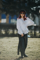 Vertical shot of a hot Caucasian woman posing in a park wearing glasses, a black hat and pants