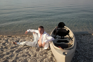 Man on beach near canoe boat on sunny summer day, sea surface in background.
