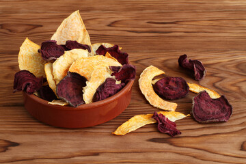 Mix of dried beetroot and pumpkin vegetable crisps lying in ceramic bowl on a wooden table. Closeup. Macro