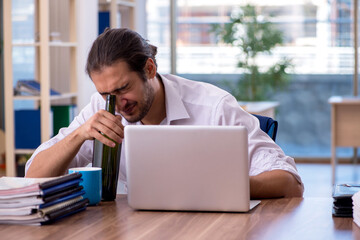Young male alcohol addicted employee working in the office