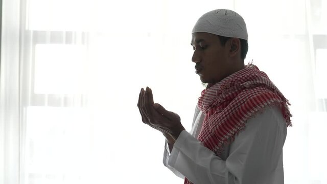 portrait of muslim man using hand to pray against white window