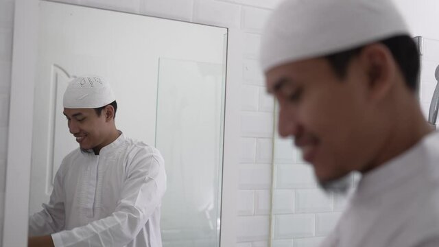 muslim asian man looking at mirror and get dressed before going to the mosque wearing islamic hat or cap