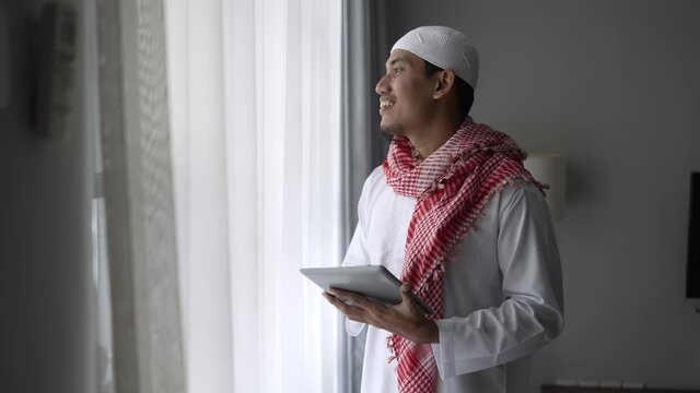 happy muslim businessman smiling while using tablet pc near window