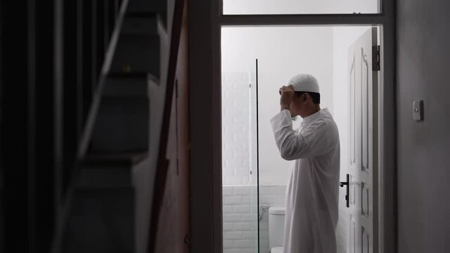 muslim asian man looking at mirror and get dressed before going to the mosque wearing islamic hat or cap