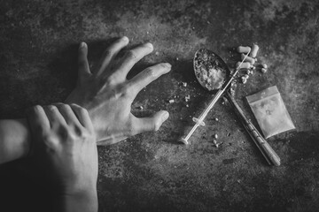 Human hand of a drug addict and a syringe with narcotic syringe lying on the floor, World anti drug day.The concept of stopping drug use. - obrazy, fototapety, plakaty