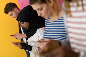 diverse teenagers use mobile devices while posing for a studio photo in front of a pink background