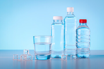 Bottles and glass of mineral water with ice cubes on blue background.