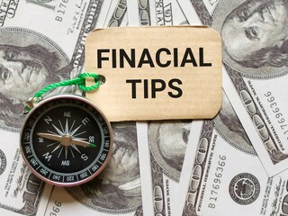 Selective focus phrase FINANCIAL TIPS written on label tag with compass and fake money. Business and finance concept.