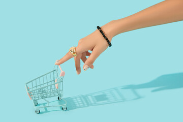 Beautiful groomed womans hand with fashionable ring holding shopping cart on blue background