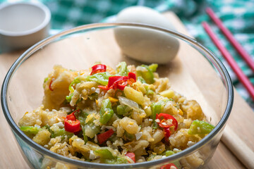 Stir fried bitter gourd with eggs and chili, in glass bowl, on light brown chopping board, Chinese style cooking