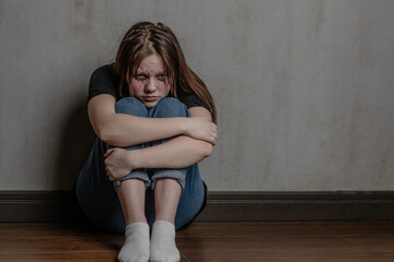 Unhappy teen girl sits on the floor near a wall. Empty space for text
