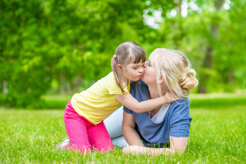 Naklejka na ściany i meble Happpy family. Little girl with special needs kisses her mother in a summer park. Empty space for text