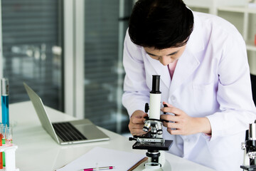 Scientific male researcher in white coat carefully seeing his specimen by microscope beside the...