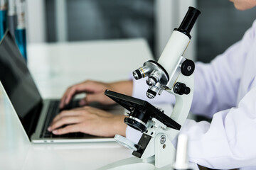 Scientific male researcher using his laptop to analyze his examining result beside the microscope in the chemistry analysis lab