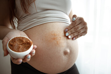 Close-up of a woman smears a scrub on her naked belly.