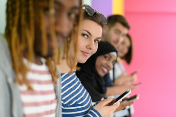 diverse teenagers use mobile devices while posing for a studio photo in front of a pink background