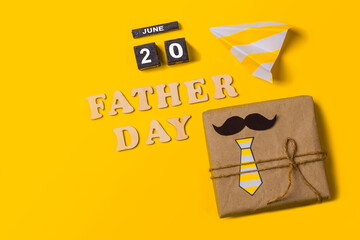 Gift box on a yellow background with the inscription in wooden letters Father's Day and the date of...