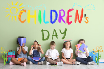 Little children with copybooks sitting on floor near color wall. International Children's Day celebration